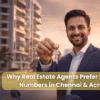 Confident Indian real estate agent in a navy suit smiling and holding house keys, standing in front of modern apartment buildings in Chennai at sunset, representing success in the property market.